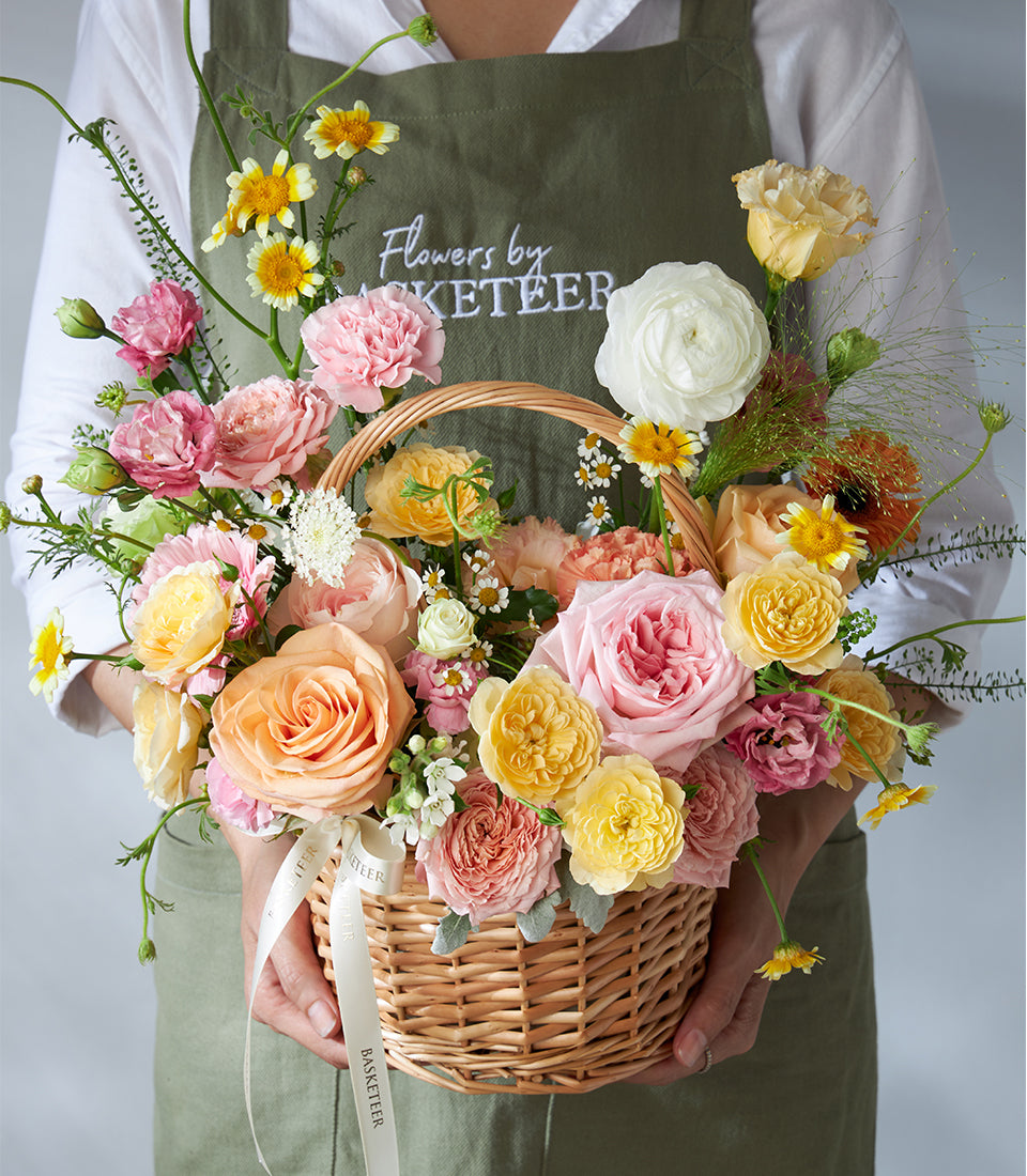 Wicker basket filled with pink, peach, yellow and white fresh roses and ranunculus, ideal for birthday flower gifts