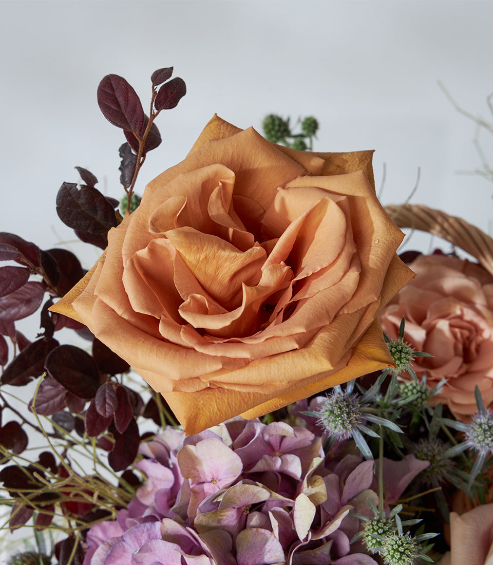 Peach rose and hydrangea arrangement in woven gift basket with thistle accents