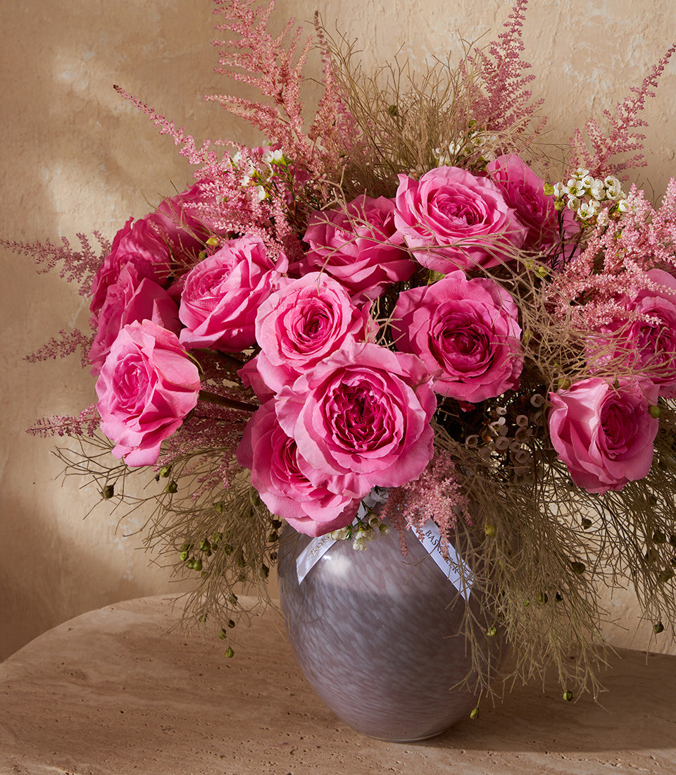 Pink rose arrangement in patterned glass vase with astilbe and dried foliage, white ribbon detail