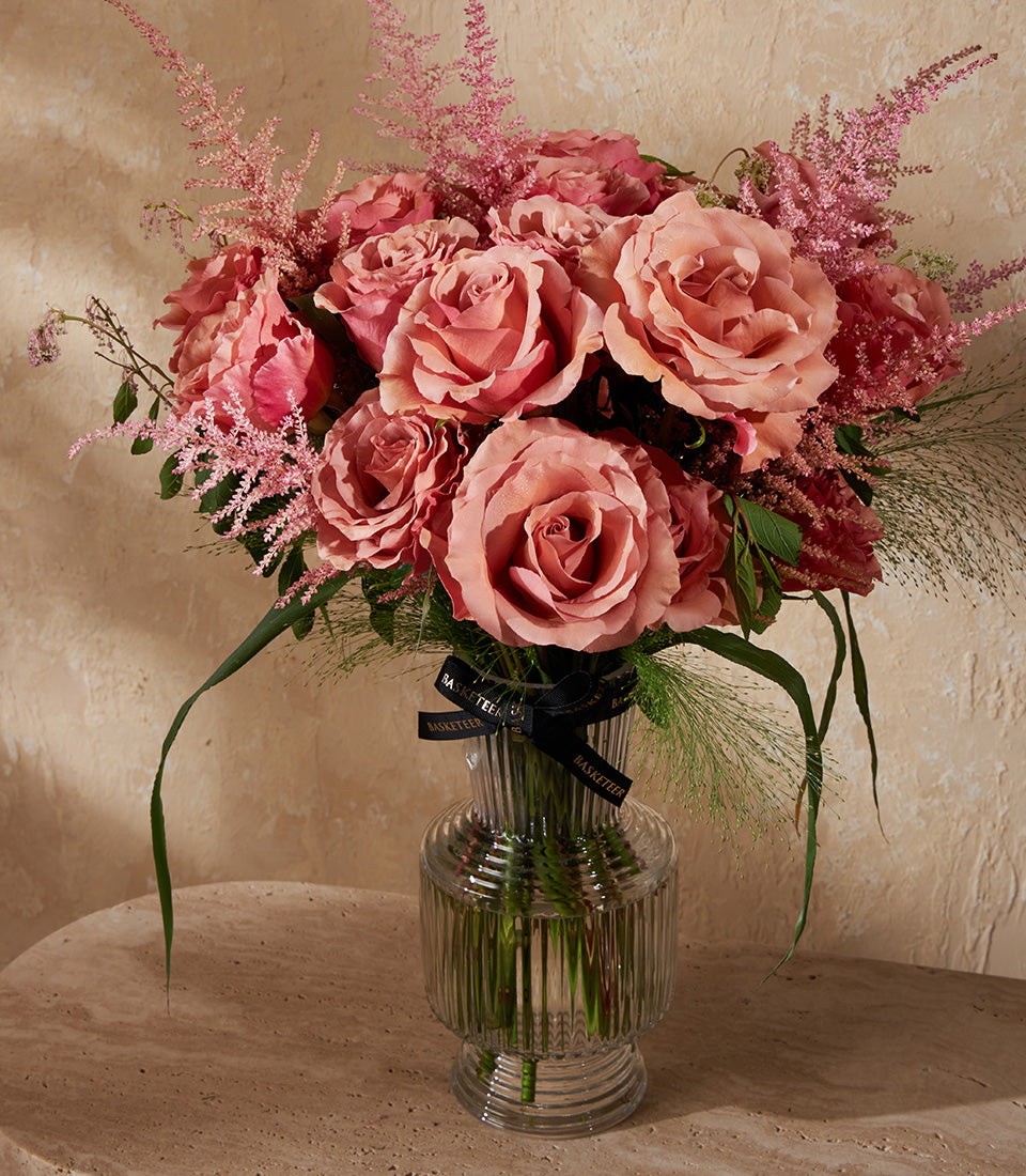 Dusty rose and deep pink premium roses with feathery astilbe in a clear glass vase with black ribbon