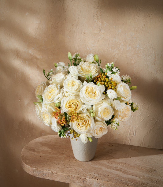 Lush white and cream roses with yellow-orange berries in light grey ceramic vase