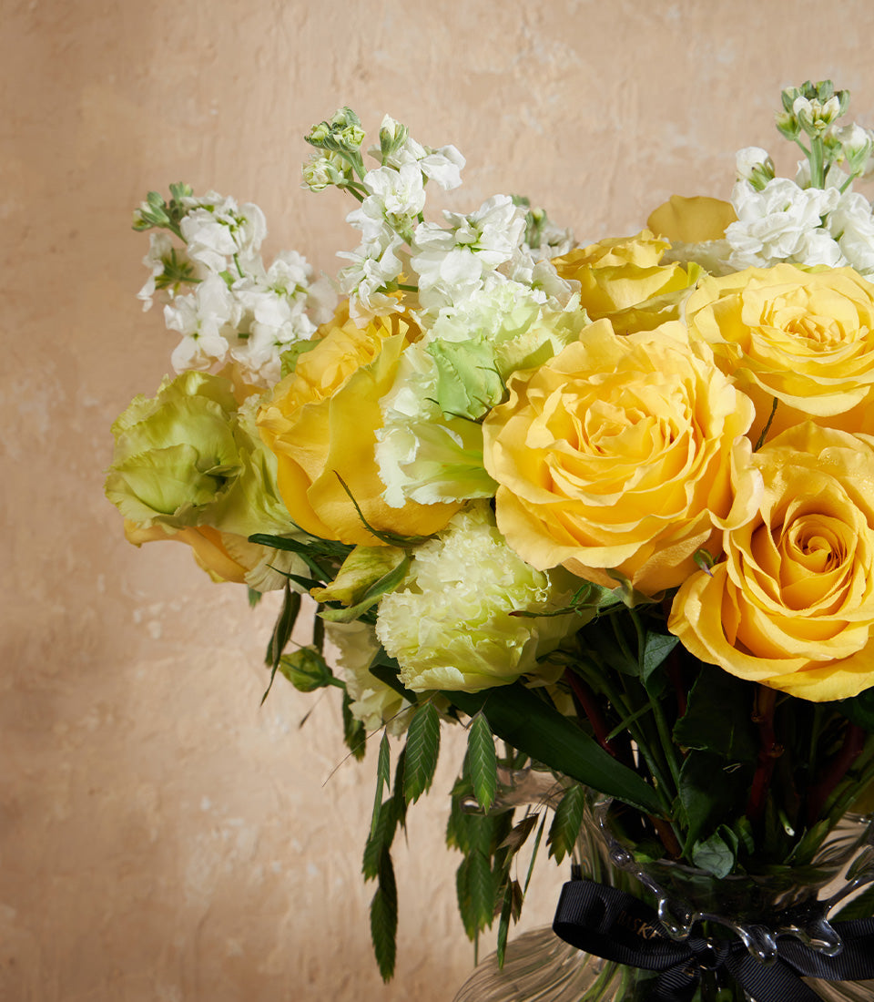 Sunlight Bloom vase with bright yellow roses, green lisianthus, and white stock flowers tied with black ribbon