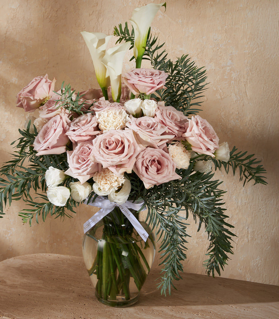 Soft pink roses and white calla lilies in elegant glass vase with cascading eucalyptus greenery