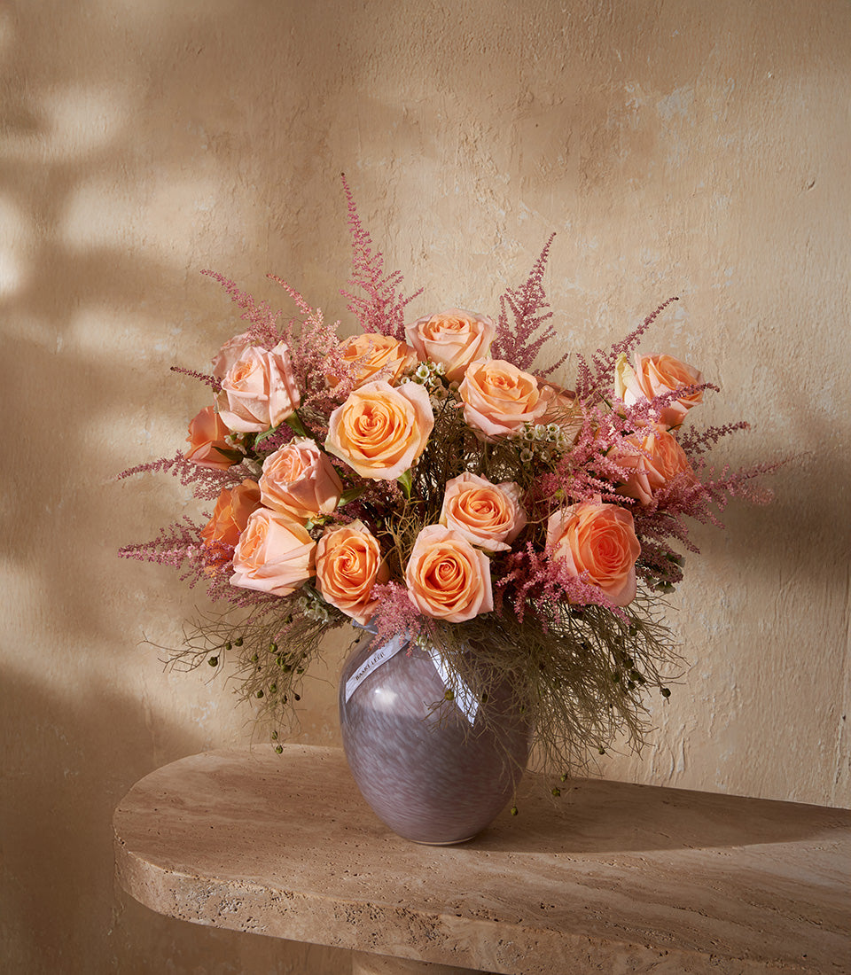 Peach roses with pink astilbe in grey-purple glass vase, premium fresh flower arrangement