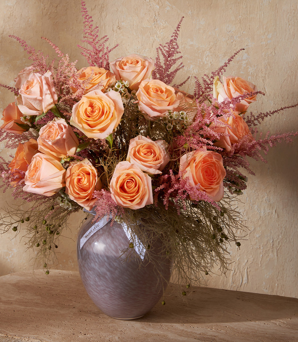 Peach roses with pink astilbe and textured branches in grey-purple glass vase