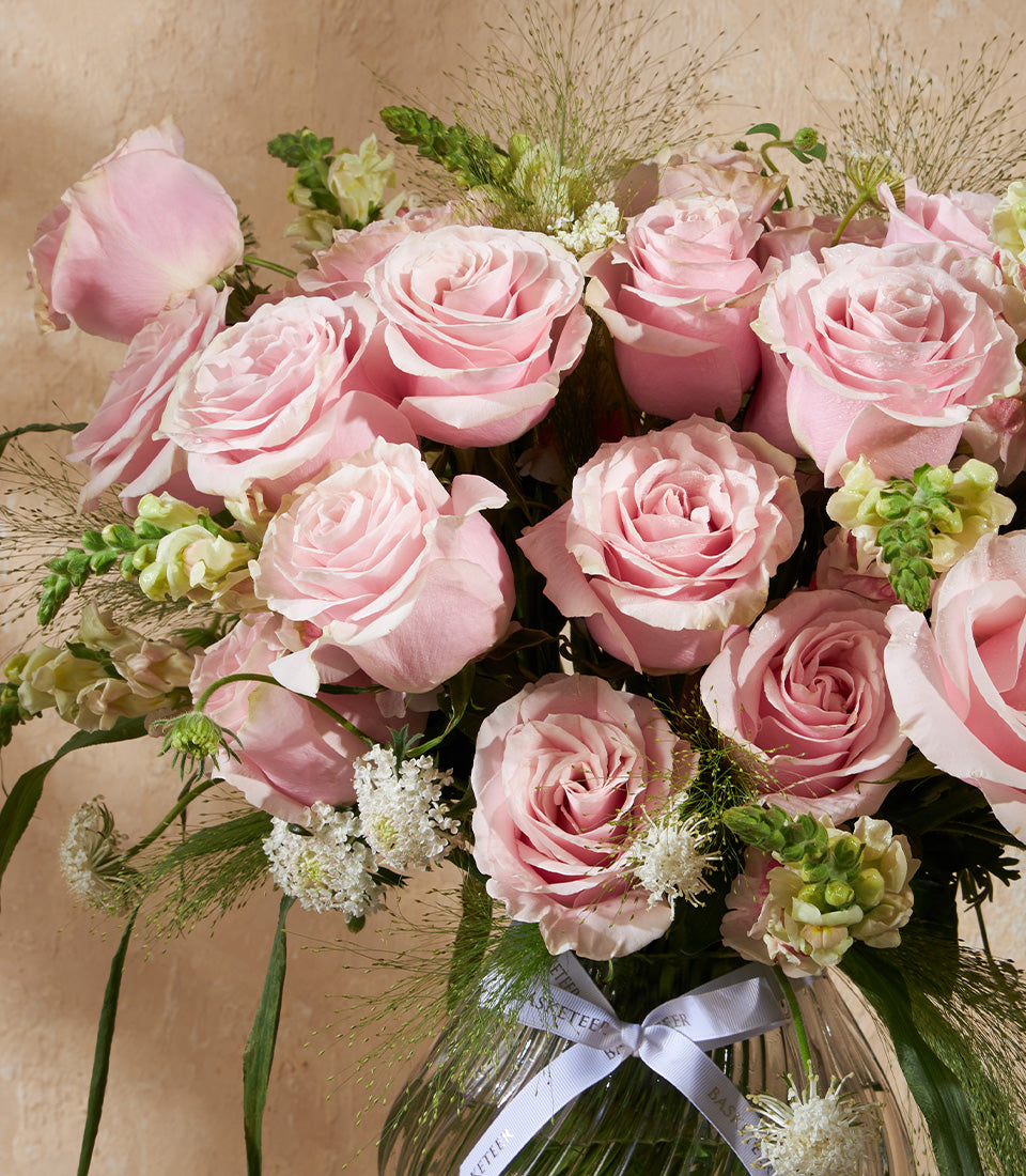 Light pink roses with white filler flowers and green foliage in clear glass vase