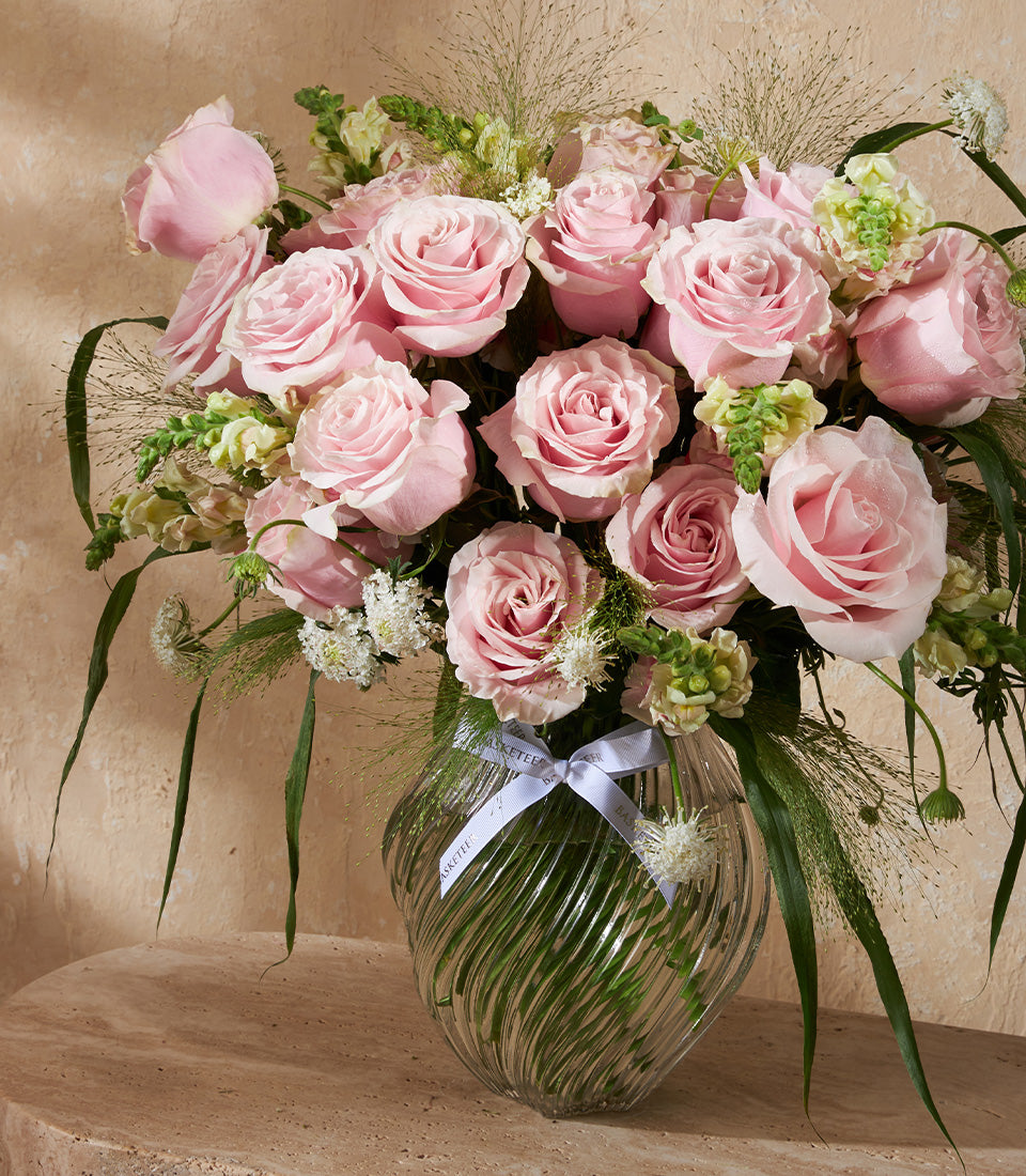 Soft pink roses with white filler flowers in textured glass vase, tied with blue ribbon