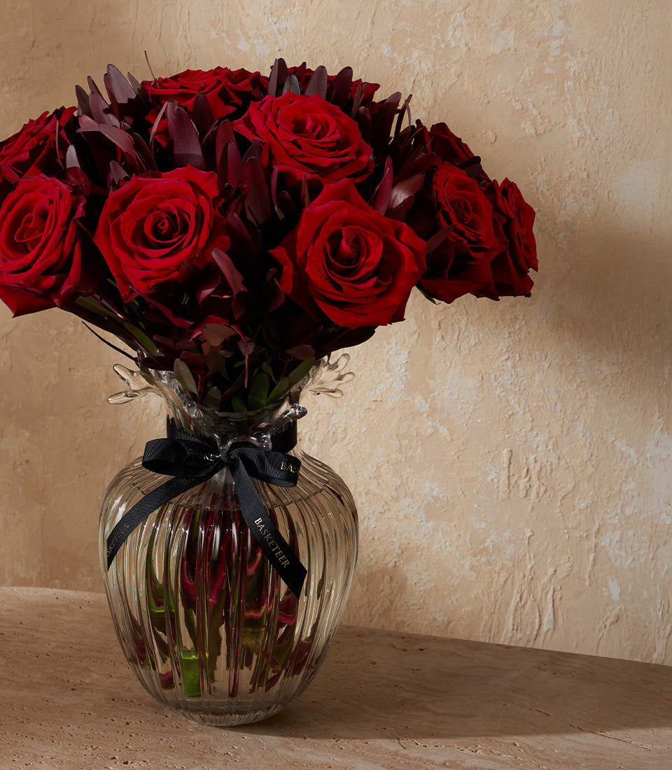 Deep red roses in clear ribbed glass vase with black ribbon bow