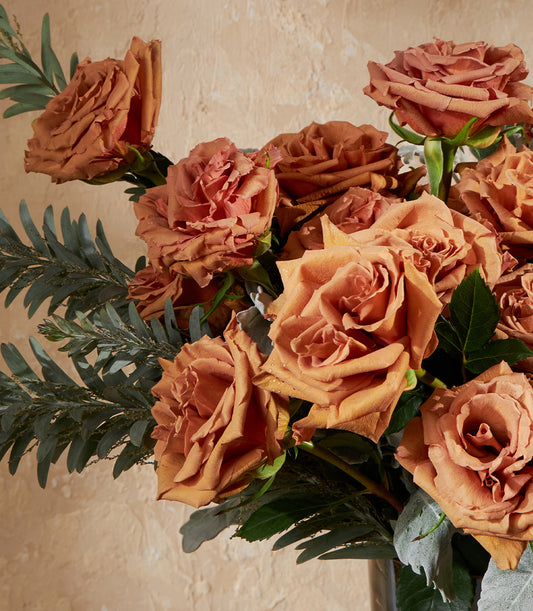 Lush orange and terracotta rose bouquet with eucalyptus greenery in golden toffee vase