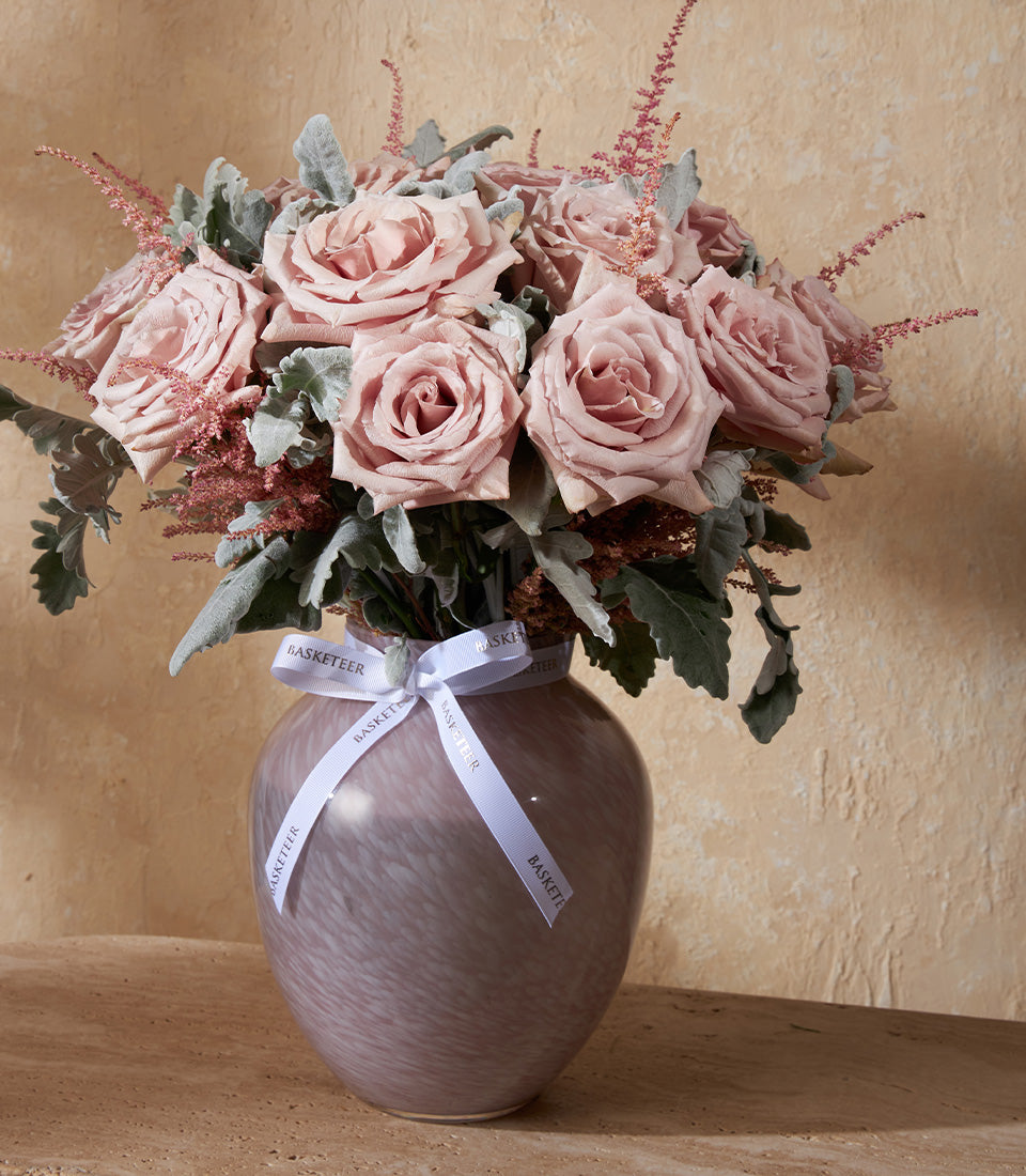 Dusty pink roses and feathery astilbe in mottled purple-grey glass vase with silvery-green dusty miller