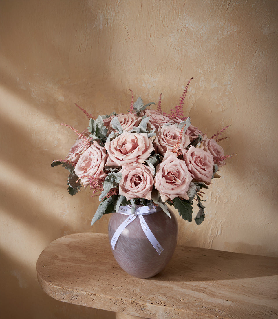 Dusty pink roses and astilbe in marbled purple-grey glass vase with silvery foliage and white ribbon