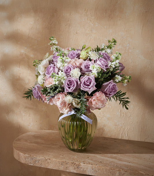 Lavender roses and pink carnations in clear ribbed glass vase with white ribbon