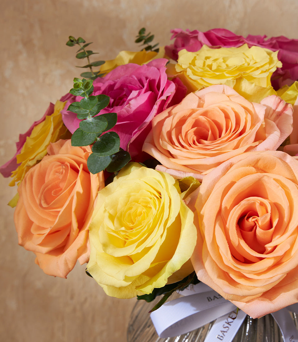 Three-color fresh rose arrangement in glass vase with eucalyptus and ribbon detail