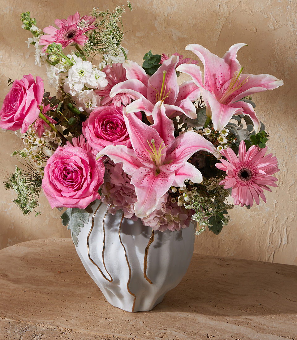 Blush pink roses, lilies, and gerberas in grey ceramic vase with gold accents