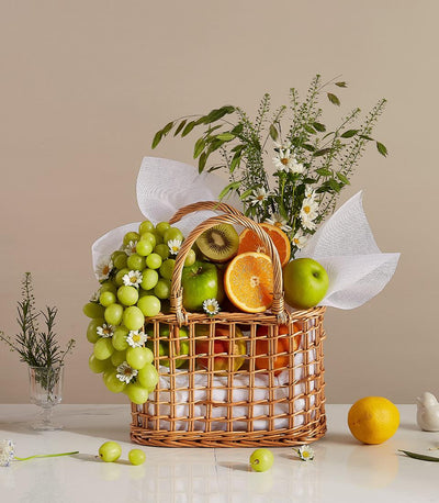 Wicker fruit gift basket with green grapes, apples, oranges, kiwi and white daisy flowers