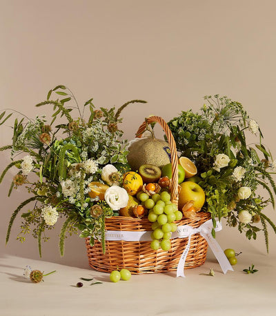 Wicker fruit and flower gift basket with fresh cantaloupe, apples, grapes, kiwi and white roses