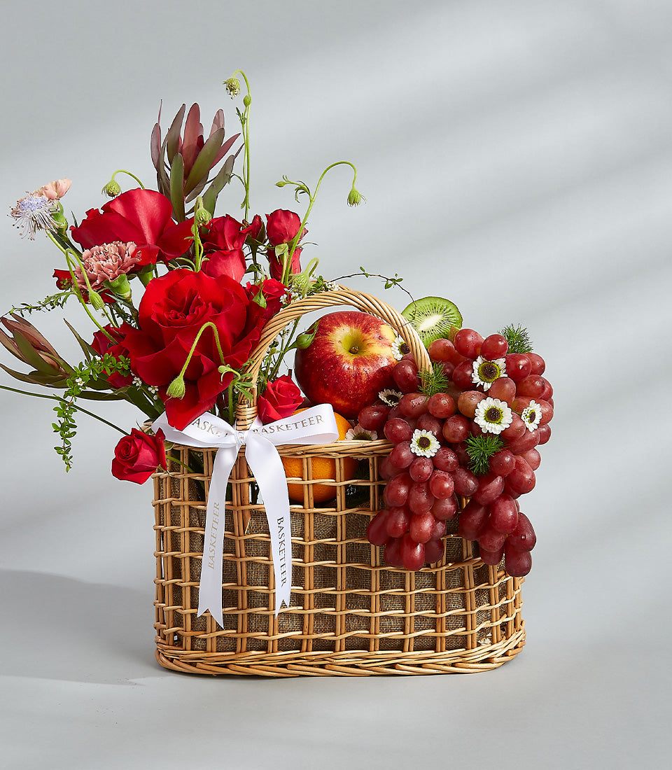 Premium red rose and fresh fruit gift basket with wicker weave and white satin ribbon, perfect for birthday celebrations