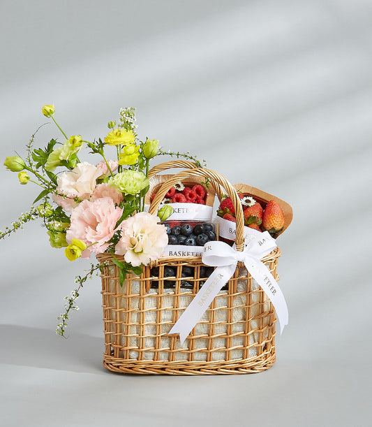Fresh fruit and flower gift basket with raspberries, blueberries, strawberries, and pink garden flowers in wicker