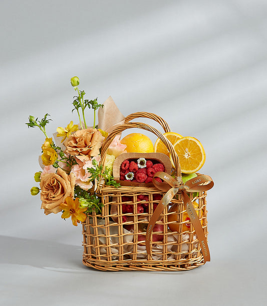 Citrus & Berry Delight wicker basket with fresh oranges, raspberries, and peach-toned roses for birthdays