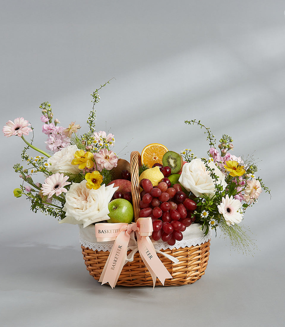 Woven wicker fruit and flower hamper with fresh roses, gerberas, citrus, and apples for gifting