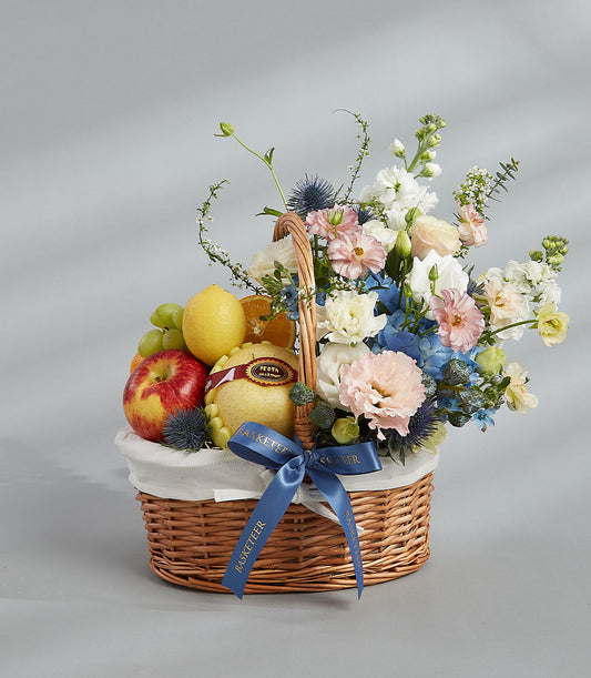 Premium wicker fruit basket with fresh apples, pears, grapes, and blue-pink flower arrangement