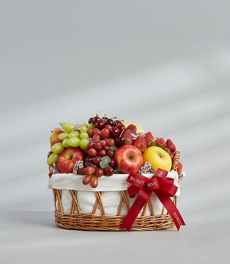 Classic woven fruit basket filled with fresh grapes, apples, strawberries and cherries with red ribbon bow