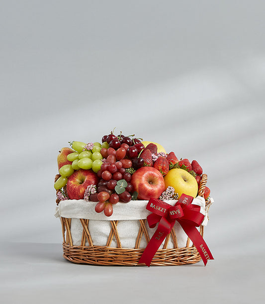 Classic woven fruit basket filled with fresh grapes, apples, strawberries and cherries with red ribbon bow