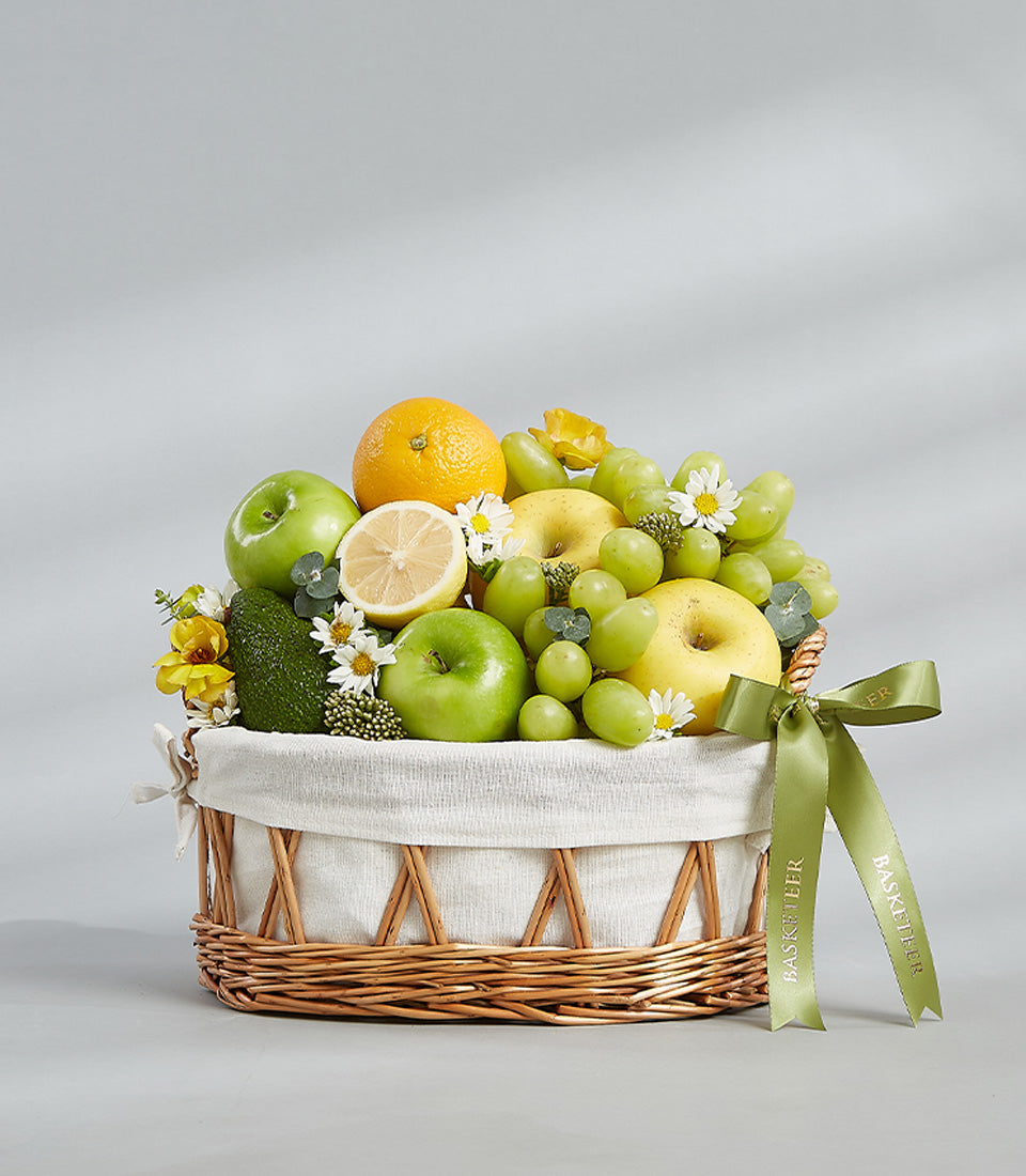Woven wicker fruit basket with fresh green apples, grapes, citrus, and white flowers with green satin ribbon