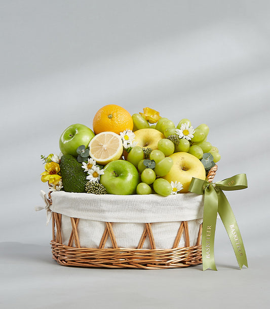 Woven wicker fruit basket with fresh green apples, grapes, citrus, and white flowers with green satin ribbon