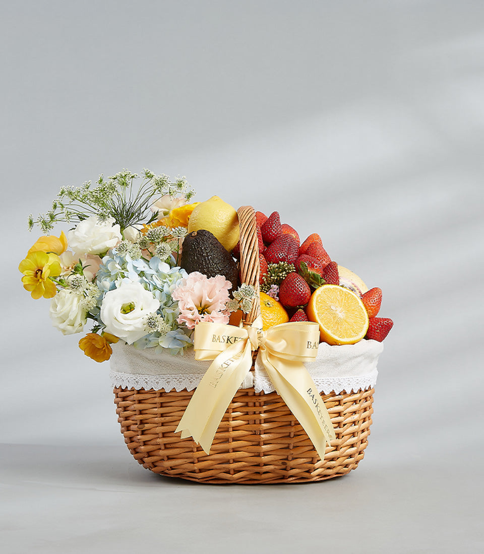 Premium fruit and flower gift basket with fresh strawberries, citrus, ranunculus, hydrangeas, and carnations in woven wicker