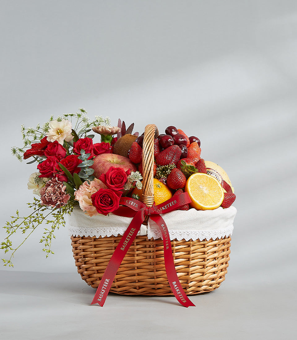 Woven wicker fruit and flower basket with fresh strawberries, cherries, roses, and carnations, tied with red ribbon