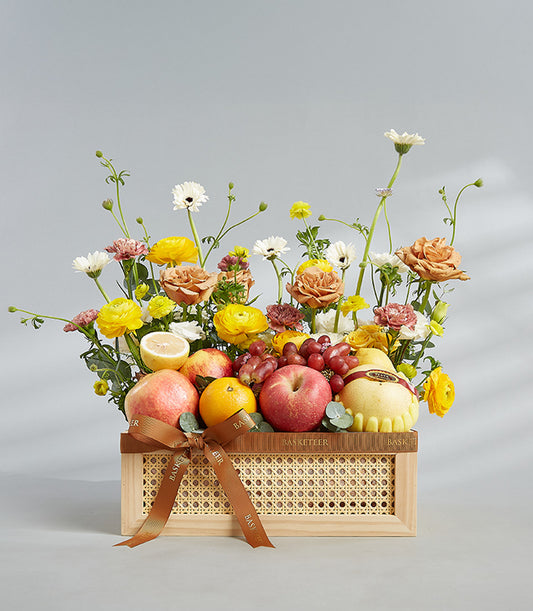 Vibrant fruit and flower arrangement in woven wooden basket with red apples, oranges, grapes, and peach roses for birthday