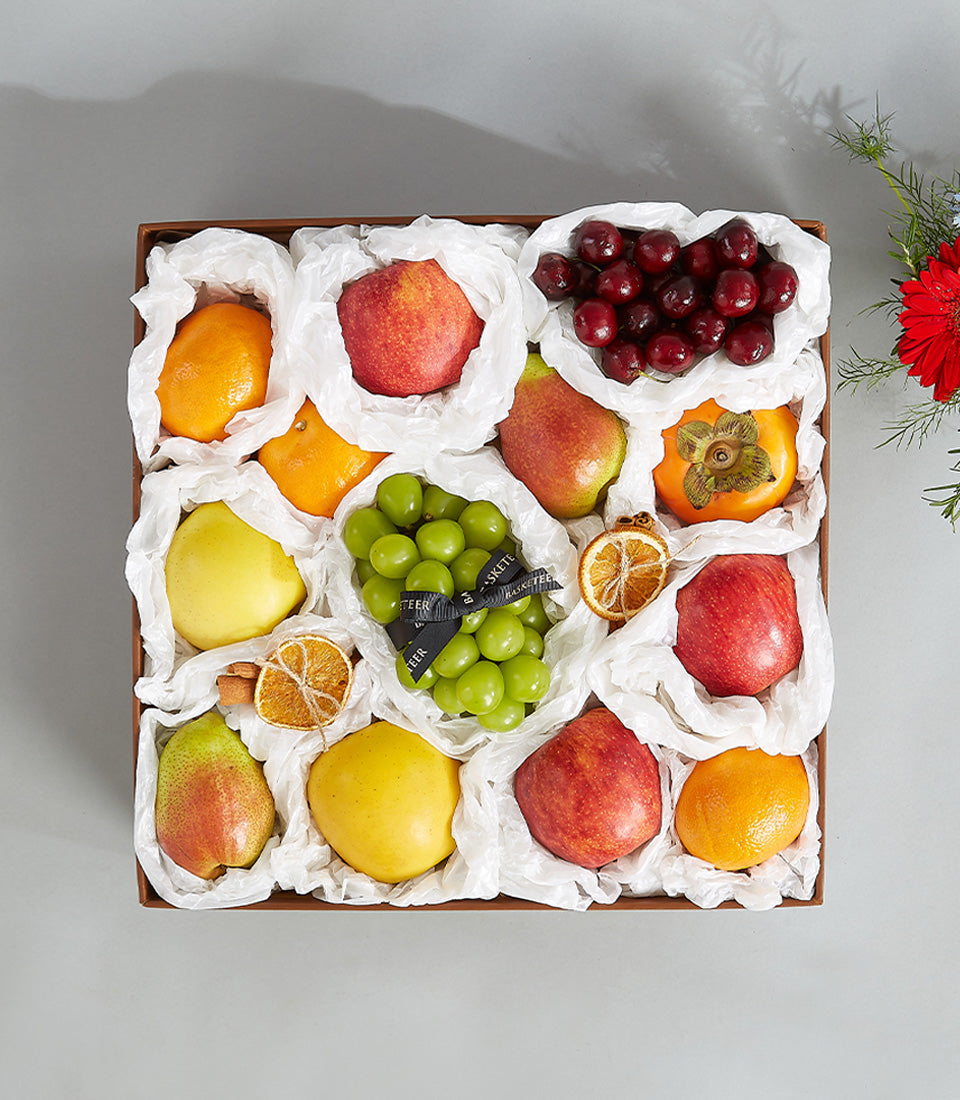 Luxury seasonal fruit gift box with wrapped apples, grapes, oranges, pears, and cherries in dark brown leather basket