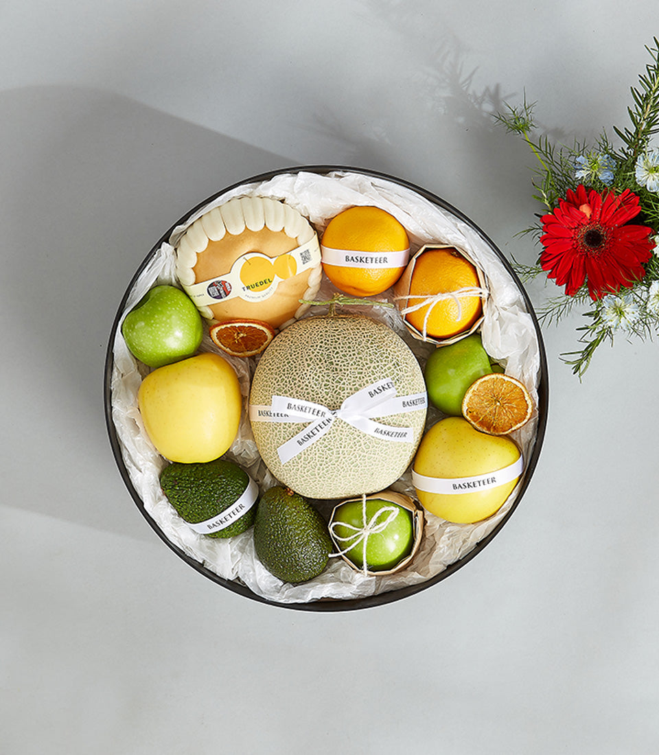 Luxury melon and citrus fruit basket with avocado and fresh flowers in black round box