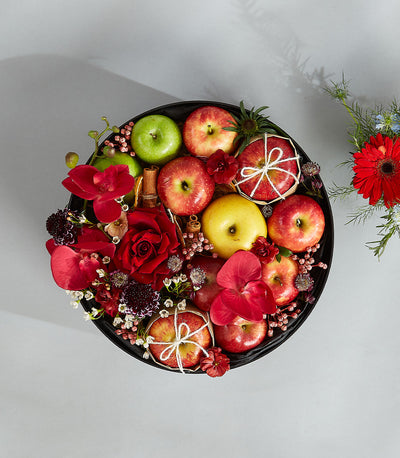 Romantic red fruit basket with red roses, orchids, apples, and cinnamon sticks in round black tray