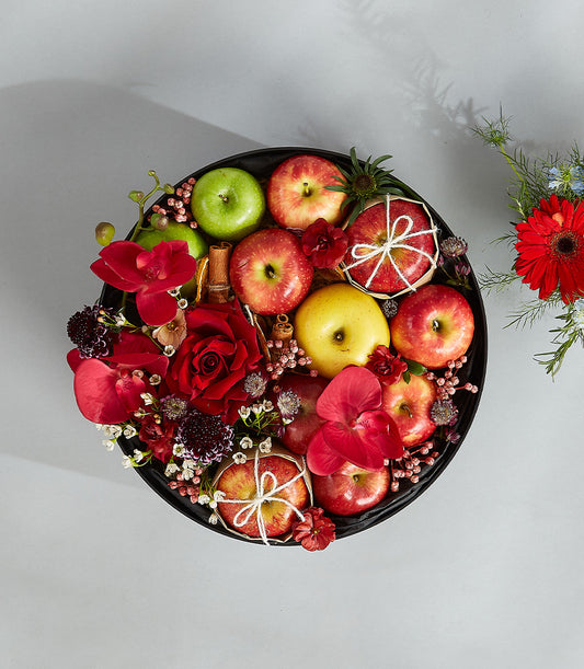 Romantic red fruit basket with red roses, orchids, apples, and cinnamon sticks in round black tray
