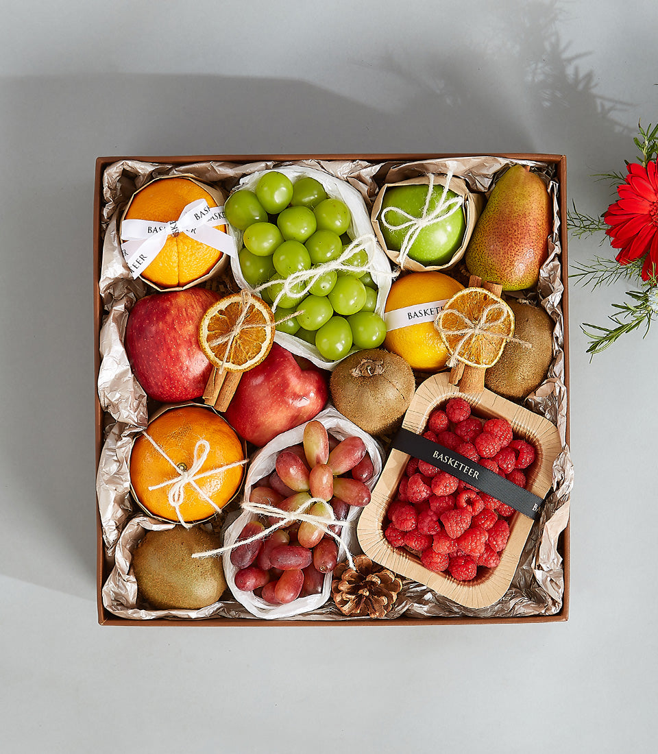 Luxury mixed fruit gift box with fresh grapes, raspberries, apples, and citrus in brown leather basket with metallic tissue