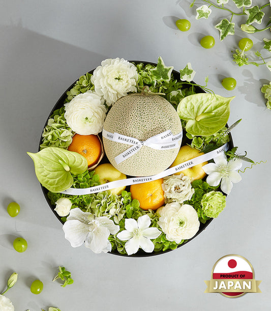 Premium Japanese fruit and flower arrangement with cantaloupe, tangerines, apples, ranunculus, and orchids in black round box