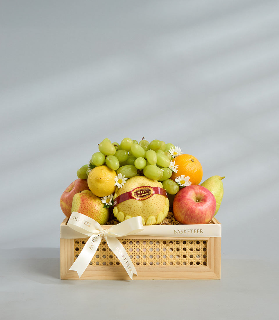 Elegant seasonal fresh fruit gift box with green grapes, apples, pears, lemons in light wooden crate with rattan panel