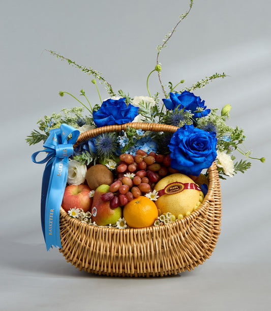 Elegant blue roses and fresh fruit in woven wicker gift basket with hydrangeas and seasonal produce