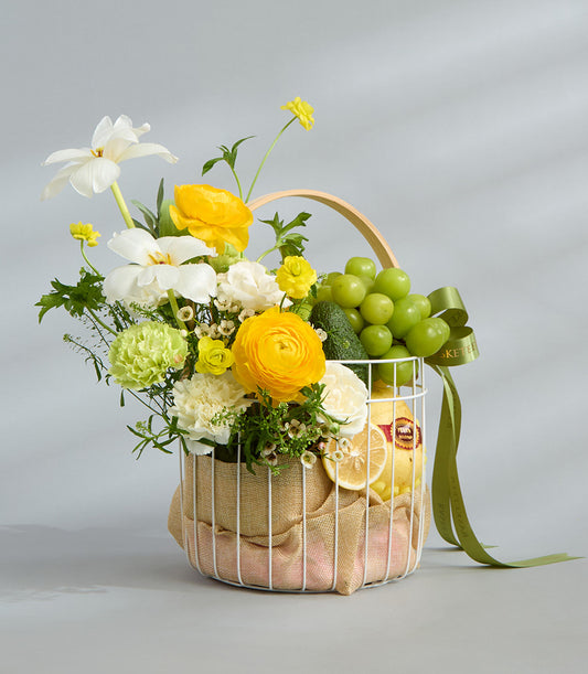Bright yellow and white floral fruit basket with daffodils, ranunculus, fresh produce, and burlap liner