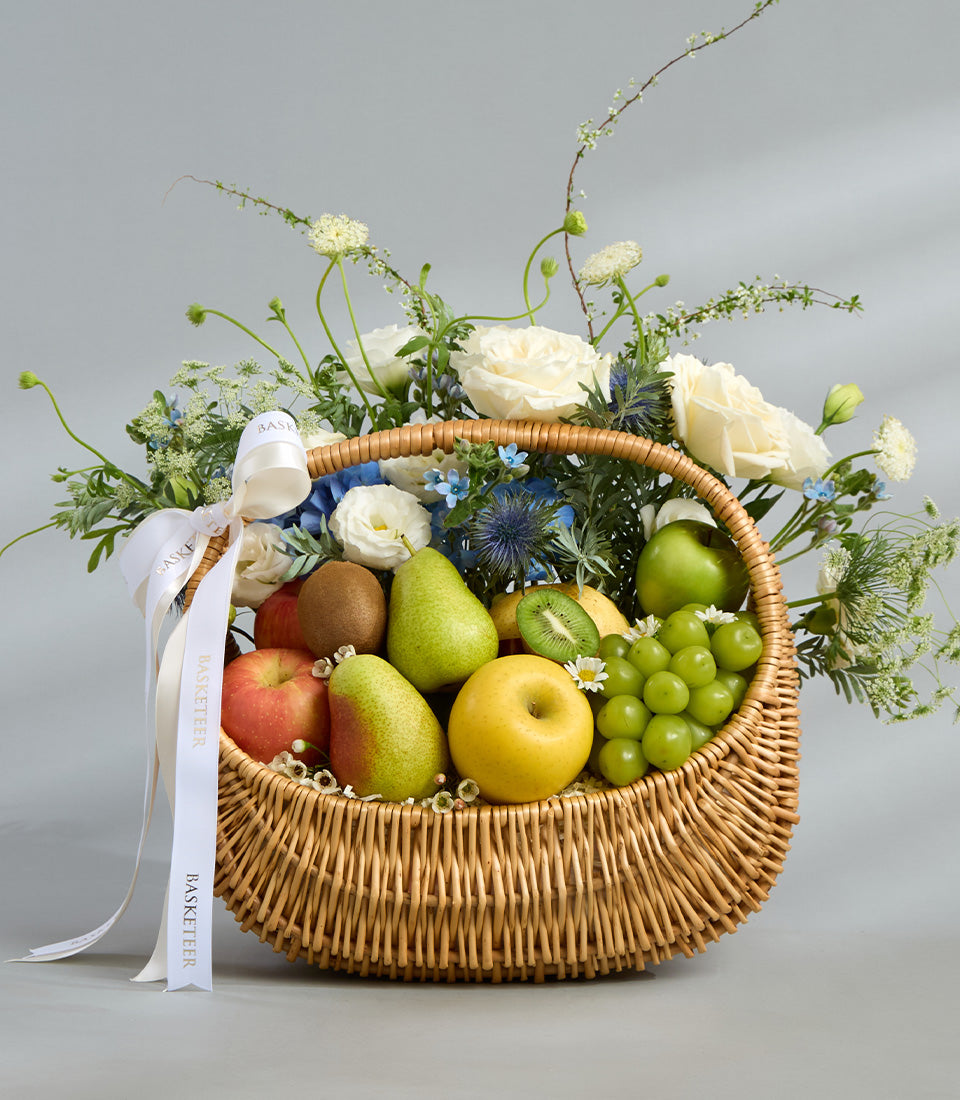 Wicker fruit basket with fresh apples, pears, grapes, and white roses with blue thistles