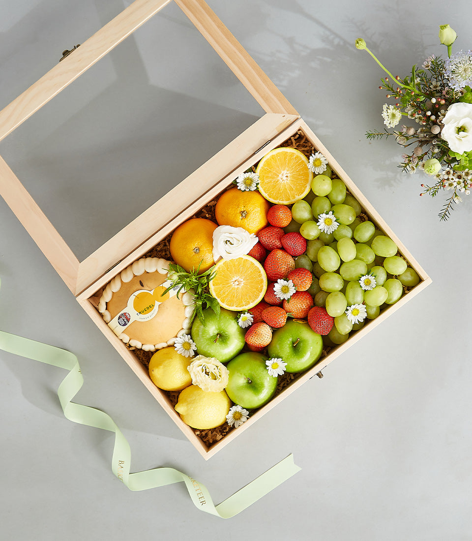Luxury wooden fruit box with fresh citrus, grapes, strawberries, and artisan tart, adorned with white flowers