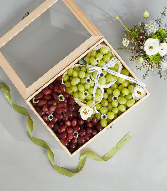 Luxury wooden gift box with dark red and green grapes, white flowers, and green Basketeer ribbon