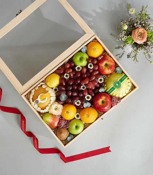 Premium wooden fruit box with fresh apples, grapes, pears, and citrus, decorated with white flowers and red ribbon