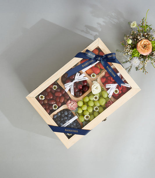 Light wooden gift box with fresh berries and grapes, topped with blue Basketeer ribbon bow