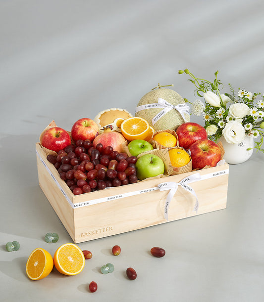 Luxury wooden crate gift box filled with fresh apples, pomegranates, oranges, grapes, and melon with white ribbon