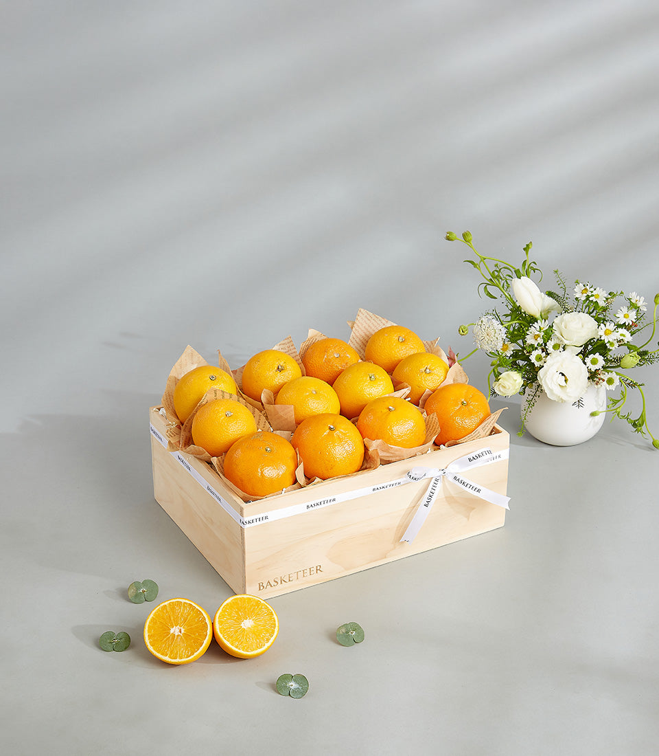 Premium wooden crate of fresh oranges with white floral arrangement and Basketeer ribbon
