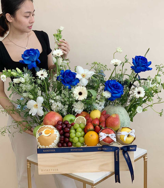 Premium blue roses and fresh fruit gift basket in wooden crate with white florals