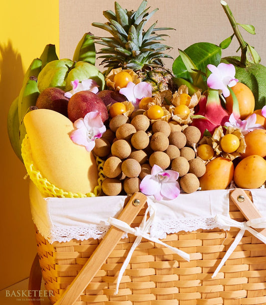 Woven tropical fruit basket with mango, dragon fruit, pineapple, bananas, longans, and orchid blossoms